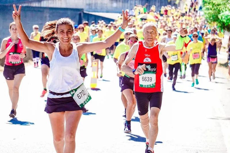 Coureuses et coureurs avec dossards lors d'une course populaire, une participante souriante qui fait le V de la victoire