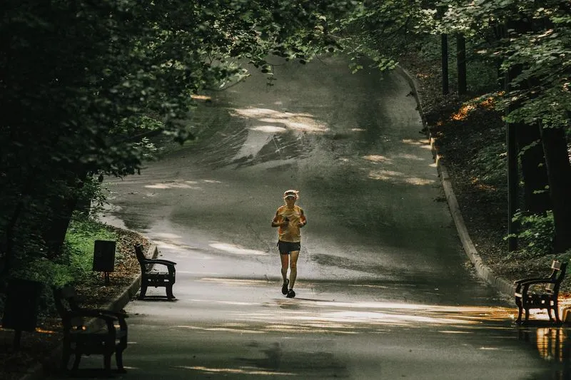 Coureuse seule sur une allée de parc ombragée, bordée d'arbres et de bancs