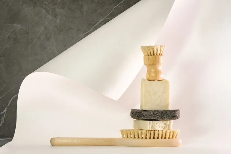 Pains de savon beige empilés entre une brosse à vaisselle et une brosse à long manche en bois à poils naturels