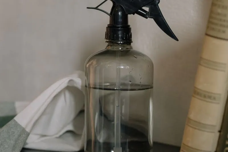 Flacon pulvérisateur transparent rempli d'un liquide clair, posé près d'un torchon en coton et de vieux livres