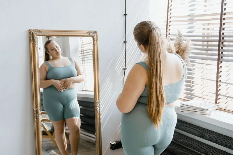 Femme en tenue de sport observant son ventre dans un miroir