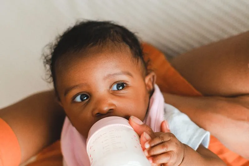 Bébé buvant son biberon, tenu contre sa mère