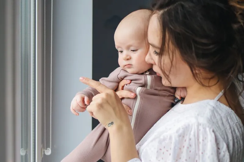 Jeune mère tenant son bébé contre elle et lui montrant la fenêtre du doigt