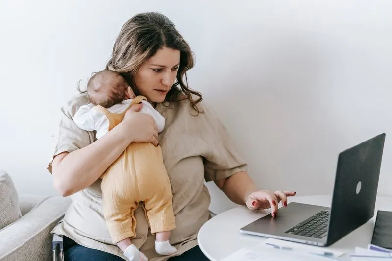 Mère au travail sur son ordinateur portable, bébé calé contre son épaule