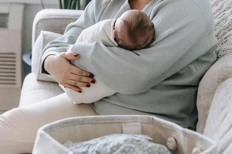 Mère assise sur un canapé, bébé endormi blotti contre elle