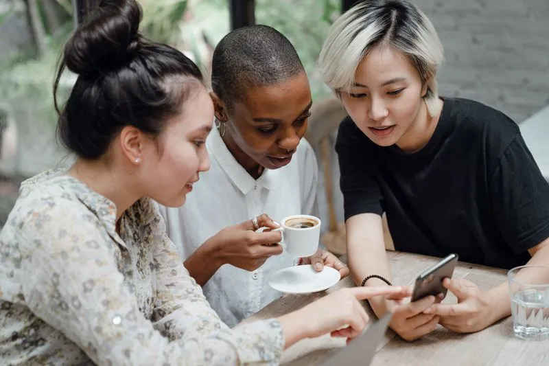 Trois amies autour d'un café, penchées ensemble sur un téléphone