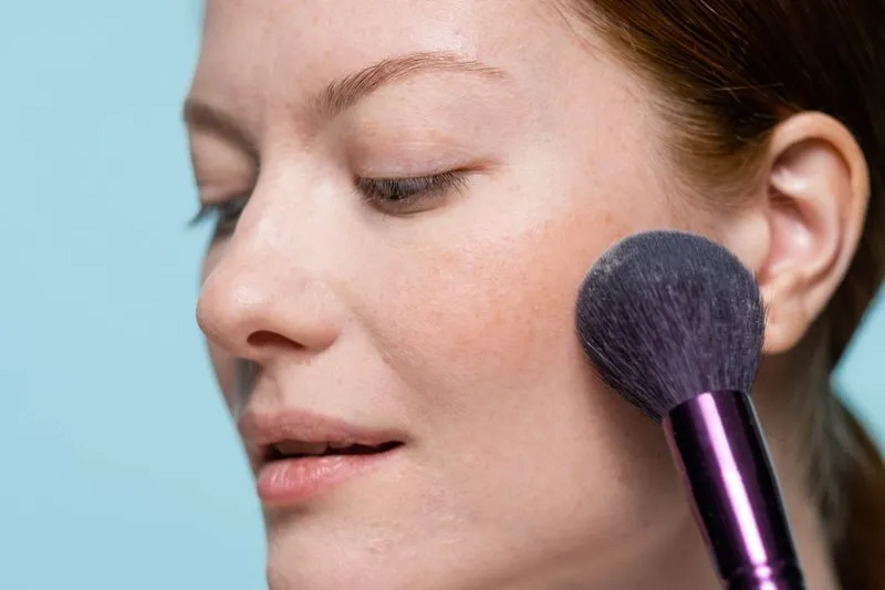 Pinceau à blush posé sur la pommette d'une femme aux taches de rousseur