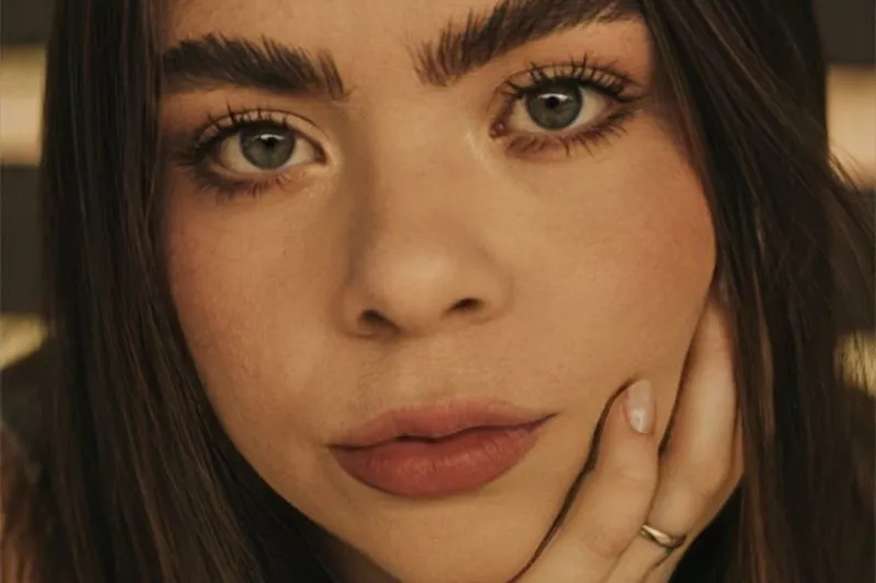 Gros plan d'une femme au teint lumineux, sourcils fournis et lèvres nude mates