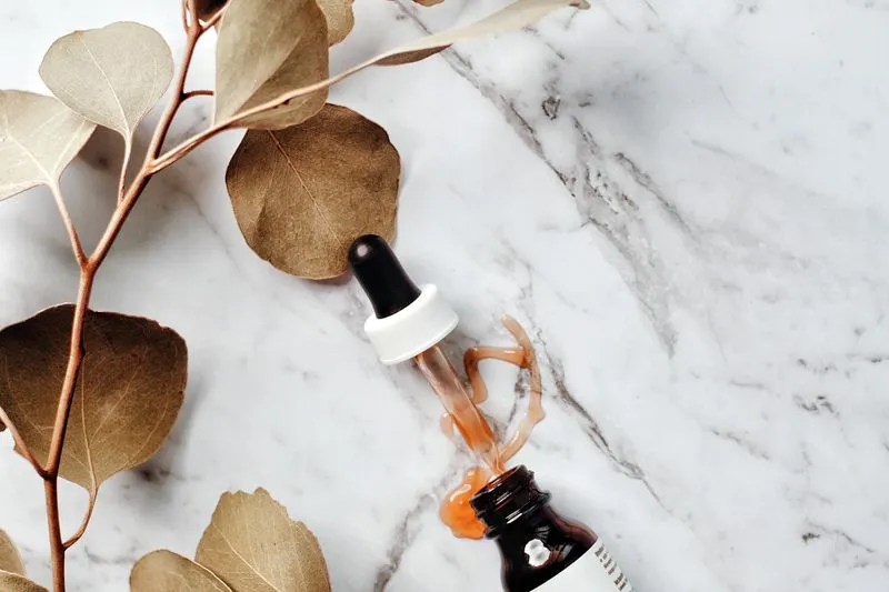Flacon de sérum ambré et sa pipette sur un plan en marbre, à côté d'une branche d'eucalyptus séchée