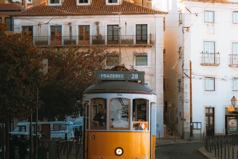Le tram 28 jaune roule vers Prazeres dans une ruelle de Lisbonne, lumière dorée du soir