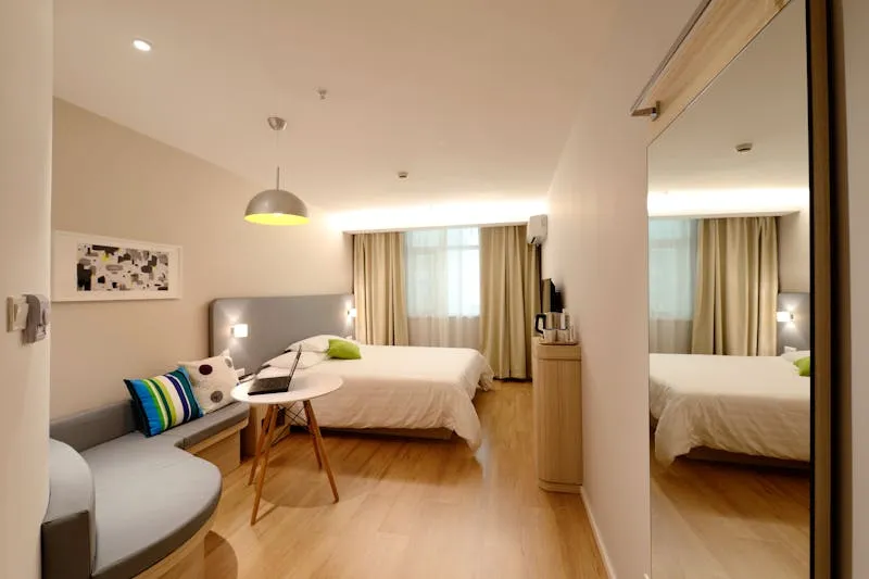 Chambre d'hôtel moderne aux tons clairs, avec lit double, banquette et grand miroir