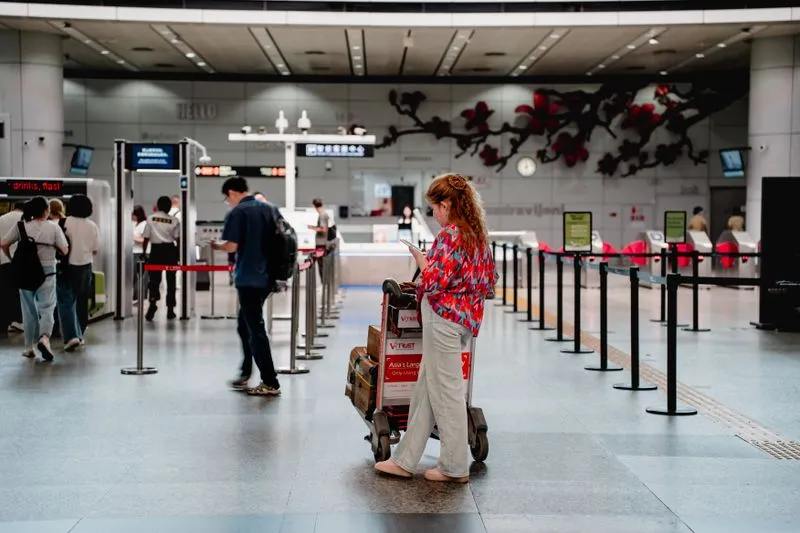 Voyageuse avec un chariot à bagages consultant son téléphone dans un hall d'aéroport