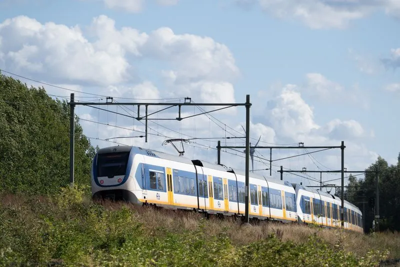 Train régional blanc, bleu et jaune roulant en pleine campagne sous un ciel nuageux