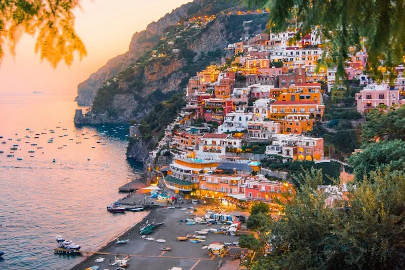 Positano au coucher du soleil, vu depuis la colline : maisons colorées étagées au-dessus de la plage et des bateaux au mouillage