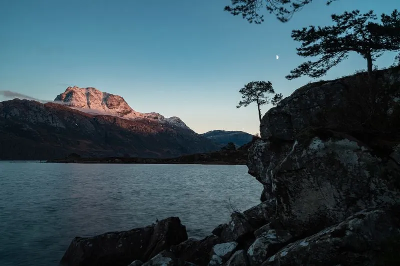 Loch et montagne des Highlands écossais au crépuscule, lune visible dans le ciel