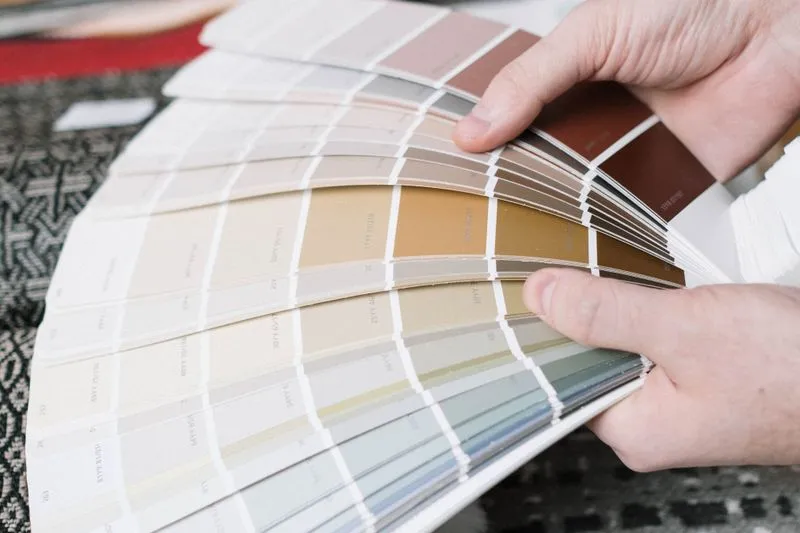 Mains qui déploient un nuancier de peinture en éventail, des blancs cassés aux bruns et aux gris-verts