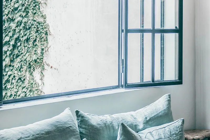 Fenêtre grande ouverte au-dessus d'une banquette aux coussins de lin vert d'eau, mur blanc