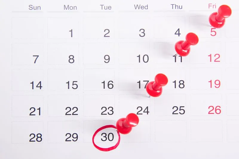 Page de calendrier où des punaises rouges marquent plusieurs jours, une date entourée au feutre rouge