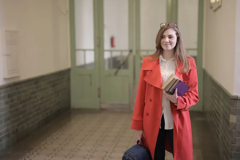 Étudiante en manteau rouge, des livres sous le bras et un sac à dos à la main, dans un couloir d'université