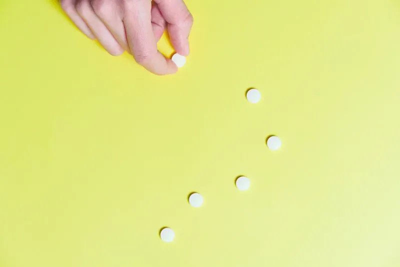 Main qui saisit un comprimé blanc parmi plusieurs posés sur un fond jaune