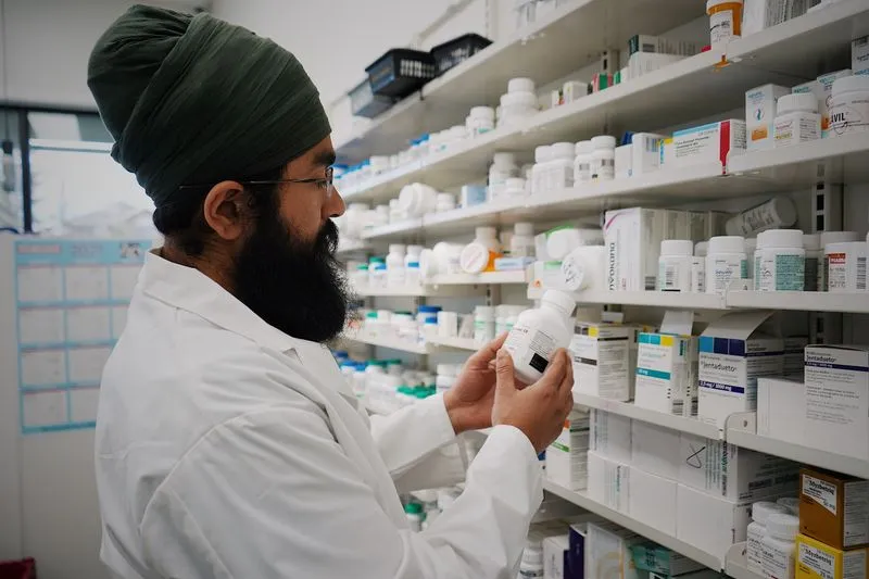 Pharmacien en blouse blanche qui vérifie un flacon de médicament devant les rayonnages de l'officine