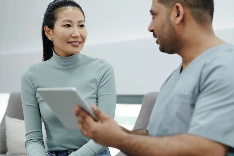 Jeune femme en consultation avec un soignant en tenue médicale qui tient une tablette