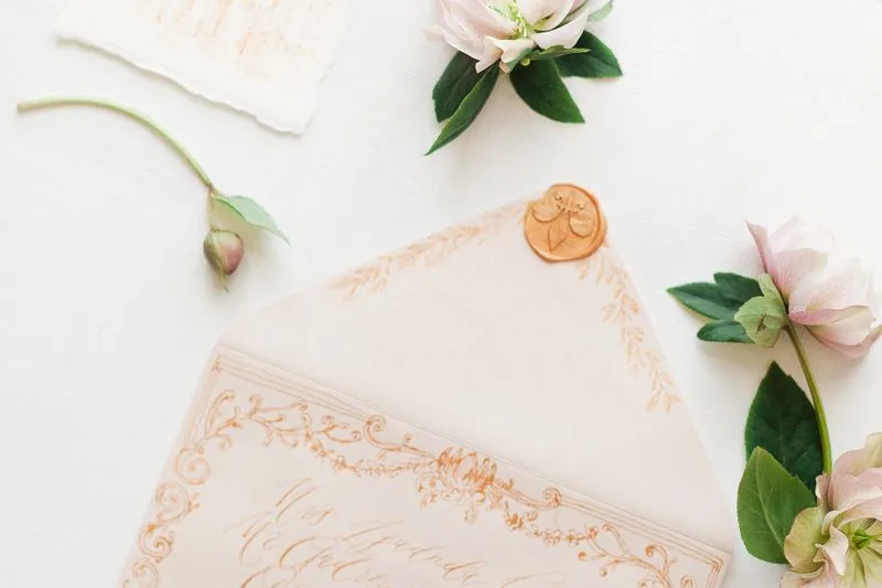 Enveloppe crème adressée à l'encre orangée en calligraphie, fermée d'un cachet de cire, entre des hellébores