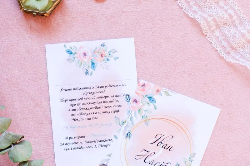 Deux faire-part rédigés en ukrainien, aux fleurs aquarellées sur fond rose, avec la date et l'adresse du restaurant
