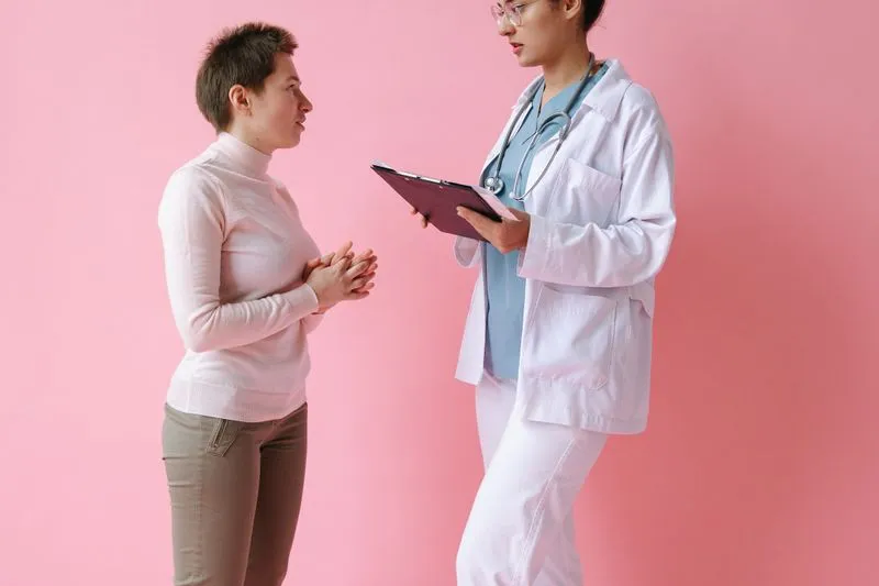 Jeune femme aux cheveux courts qui s'explique face à une médecin tenant un porte-bloc