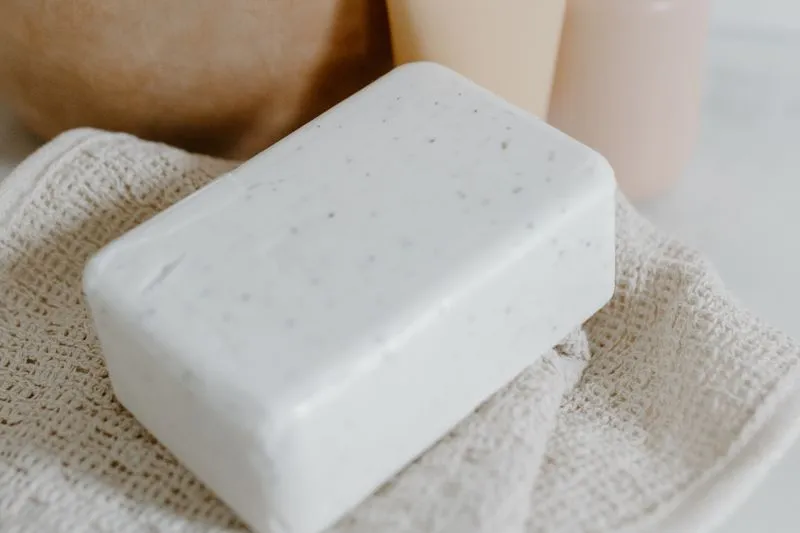 Pain de savon blanc posé sur une serviette en coton nid d'abeille, devant deux flacons clairs