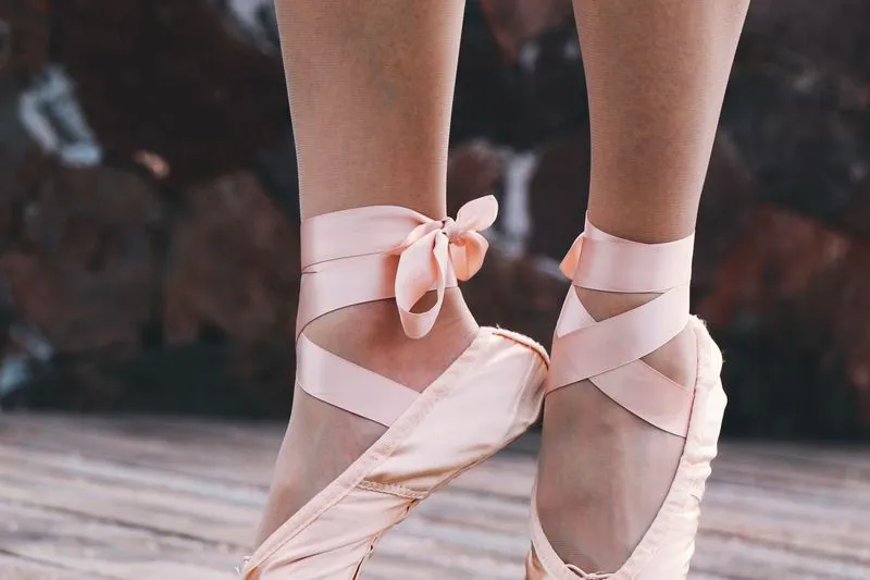 Gros plan sur des chaussons de danse rose pâle, rubans de satin croisés et noués autour des chevilles