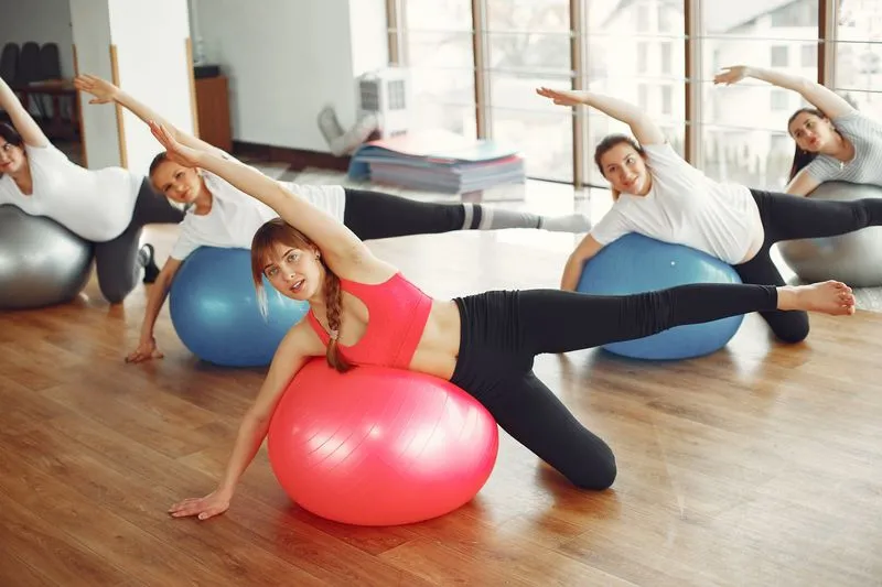 Cours de gym sur gros ballons : des femmes penchées sur le côté, un bras tendu au-dessus de la tête