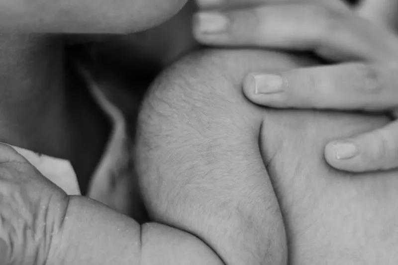 Gros plan en noir et blanc d'un nouveau-né blotti en peau à peau contre la poitrine de sa mère, qui le tient de la main