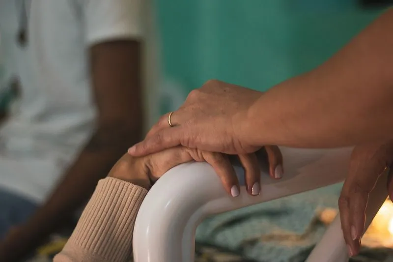Une main posée sur celle d'une personne qui serre la barre blanche d'un lit d'hôpital