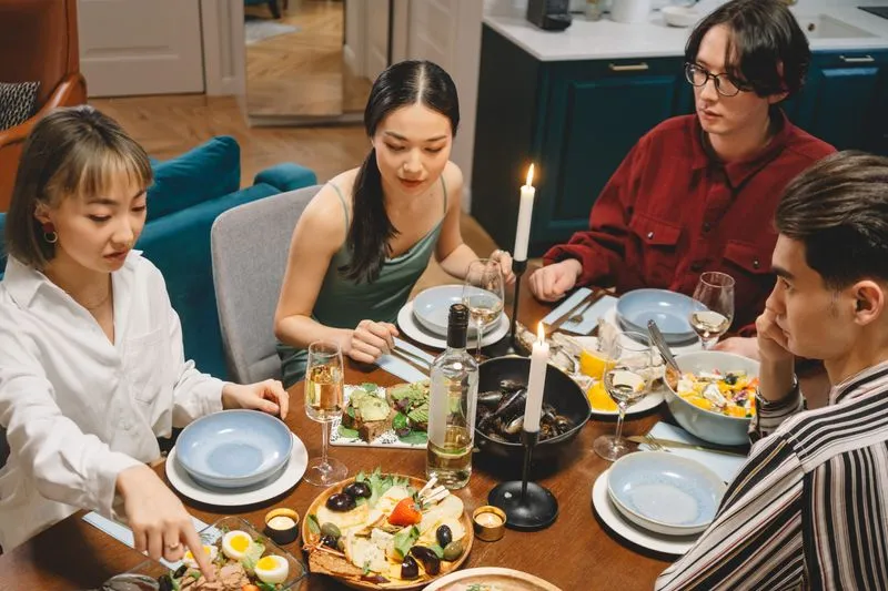 Groupe de jeunes amis autour d'une table éclairée aux bougies, qui partagent plusieurs plats et des verres de vin blanc