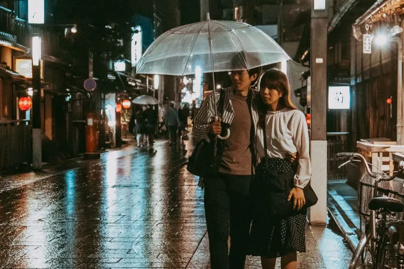 Couple serré sous un parapluie transparent dans une ruelle pavée et mouillée, la nuit