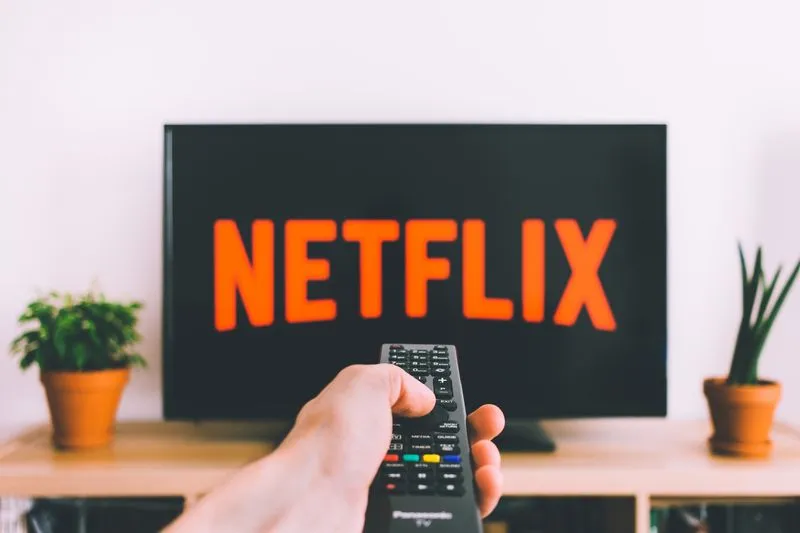 Main tendant une télécommande vers un téléviseur qui affiche le logo Netflix