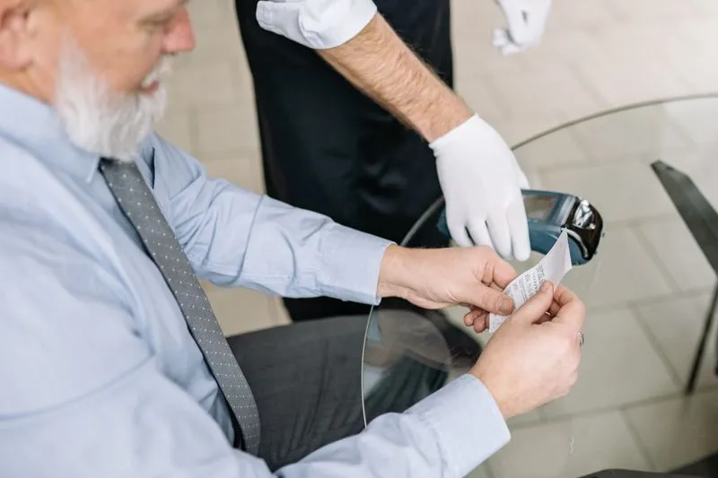Client qui relit son ticket pendant qu'un serveur en gants blancs tient le terminal de paiement
