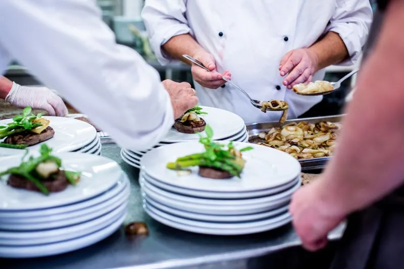 Cuisiniers en veste blanche qui dressent à la chaîne des assiettes identiques garnies d'asperges vertes, sur des piles d'assiettes