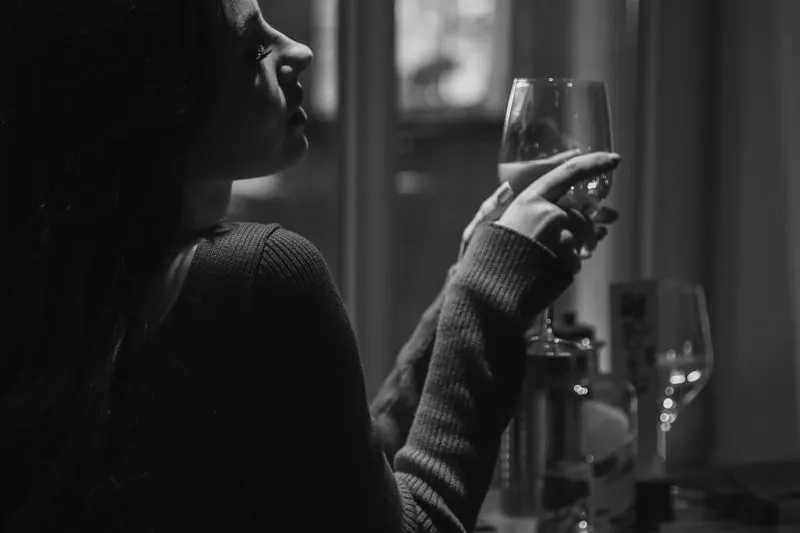 Femme attablée seule, un verre de vin à la main, en noir et blanc