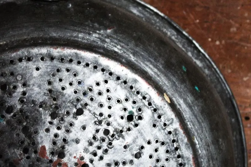 Gros plan sur le fond d'une vieille passoire en métal, percé de dizaines de petits trous, posée sur une table en bois