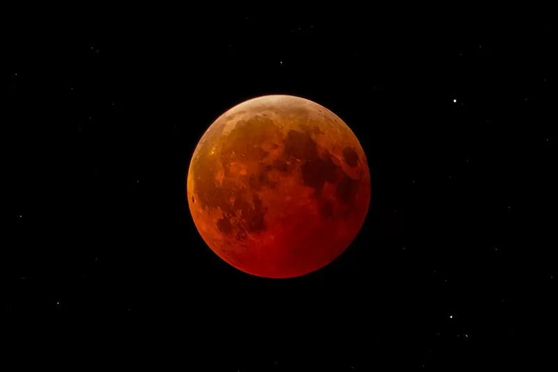 Pleine Lune rouge cuivré parmi quelques étoiles, dans un ciel noir, pendant une éclipse totale de Lune