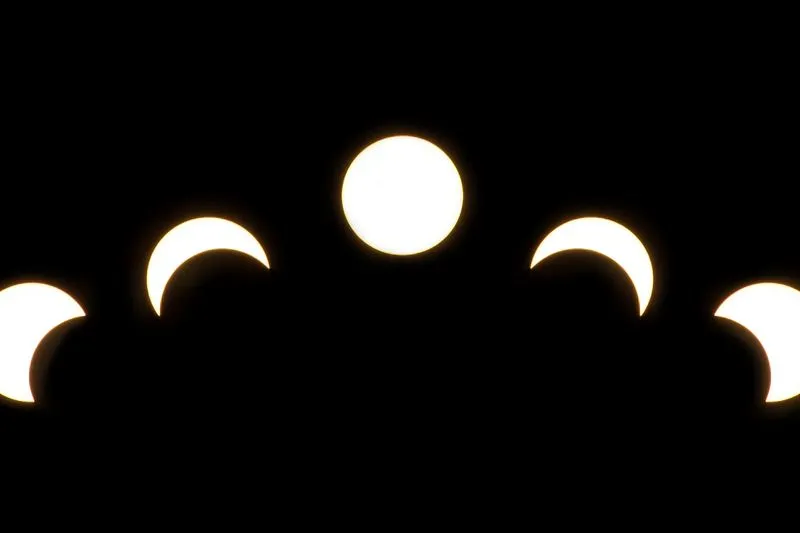 Montage de cinq vues d'une éclipse de Soleil sur fond noir : le disque solaire entier au centre, entamé en croissant de part et d'autre