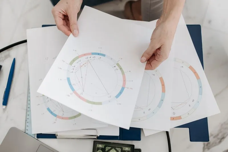 Mains qui tiennent plusieurs thèmes natals imprimés, avec leur roue des maisons en couleurs, au-dessus d'un bureau