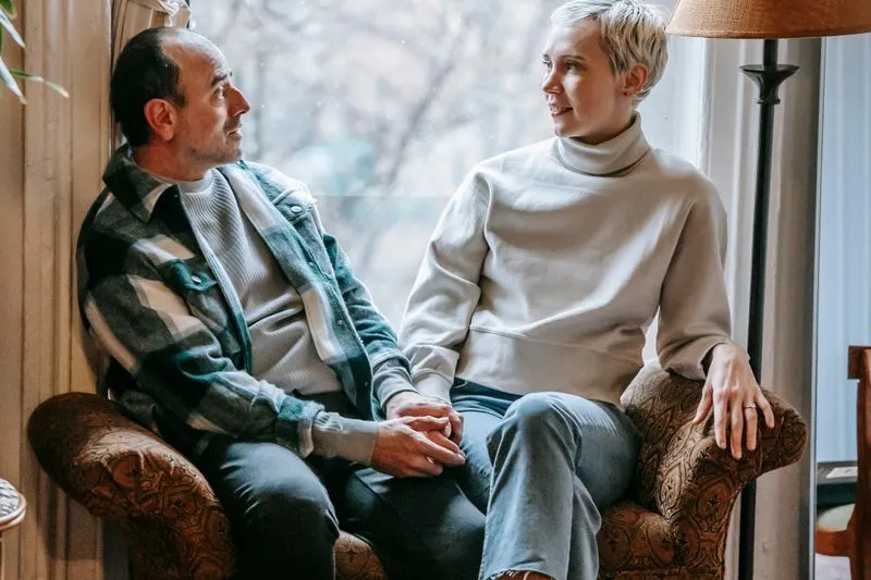 Couple assis dans un fauteuil près d'une fenêtre, main dans la main, qui discute calmement