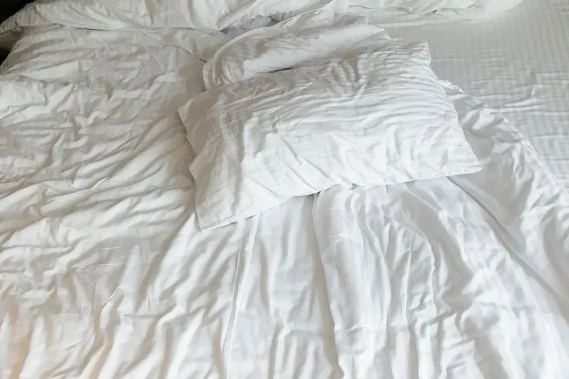 Oreiller blanc posé sur un lit défait aux draps froissés