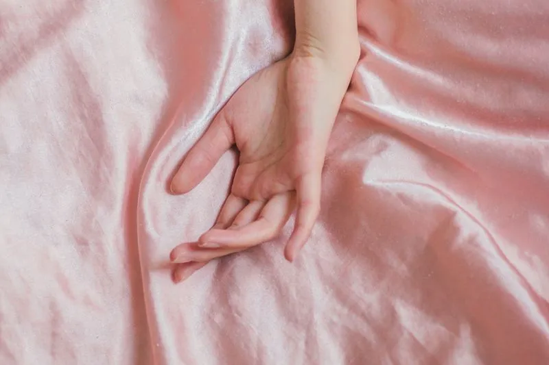 Main de femme posée sur un drap de satin rose