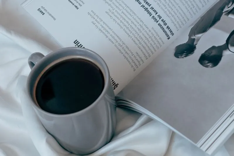 Tasse de café posée sur un magazine ouvert, au milieu de draps blancs
