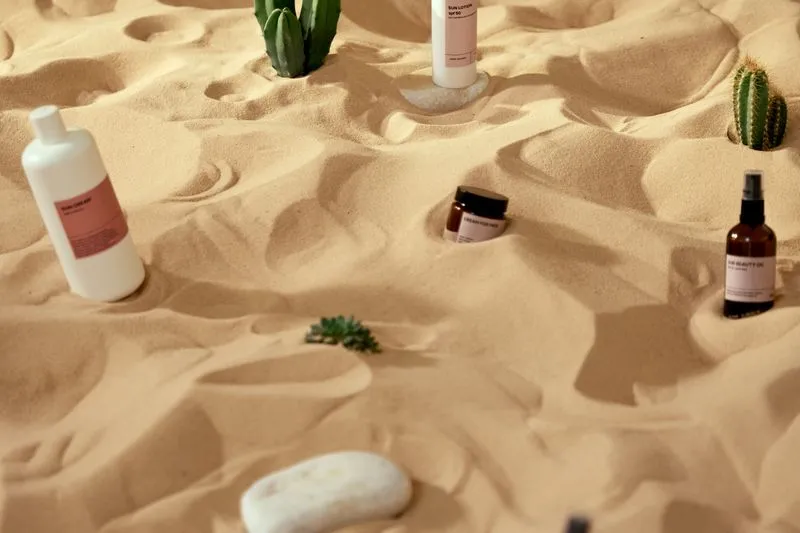 Flacons de crème et de lait solaires plantés dans le sable, en plein soleil