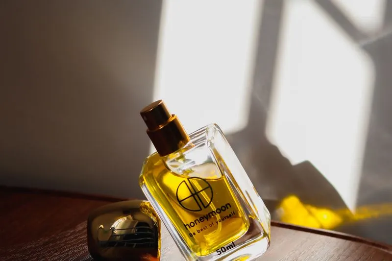 Flacon de parfum doré posé sur un plateau en bois, traversé par un rayon de soleil